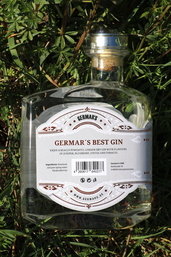 Rückseite der Germar's Best Gin Flasche mit Etikett und Botanicals-Auflistung, im Grünen liegend, mit Fokus auf die Produktdetails.