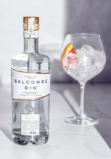 Salcombe Gin Flasche auf Marmortisch, daneben ein Glas mit Eiswürfeln und Grapefruitscheibe.