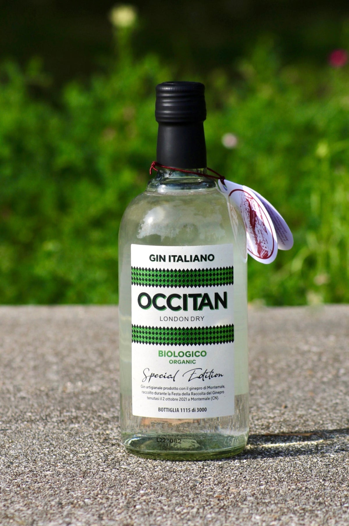Flasche Occitan London Dry Gin Biologico auf Steinfläche mit grünem Hintergrund.