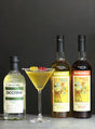 Flaschen von Occitan Gin und Bordiga Vermouth neben einem goldgelben Golden Ermine Cocktail im Martiniglas mit Gummibärchen-Garnitur.