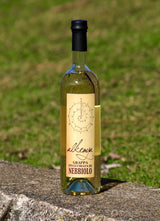 "Flasche Grappa Invecchiata di Nebbiolo mit goldfarbenem Etikett, stehend auf einer Mauer vor einer grünen Wiese.