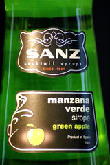 Nahaufnahme des Frontetiketts von Sanz Grüner Apfel Sirup mit weißem Logo und grünem Apfelsymbol auf schwarzem Hintergrund.
