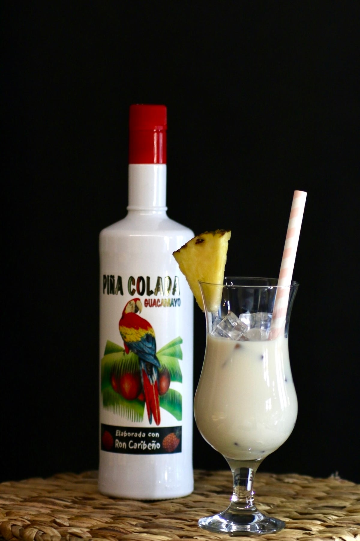 Guacamayo Piña Colada Fertigcocktail mit Flasche und dem cremigen Piña-Colada-Drink im Hurricane-Glas mit Ananasstück.