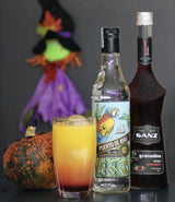Halloween Sunset Cocktail mit Rum Puerto de Ayas, Grenadine Sirup Sanz und Kürbis vor einer Halloween Hexe.
