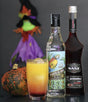 Halloween Sunset Cocktail mit Rum Puerto de Ayas, Grenadine Sirup Sanz und Kürbis vor einer Halloween Hexe.