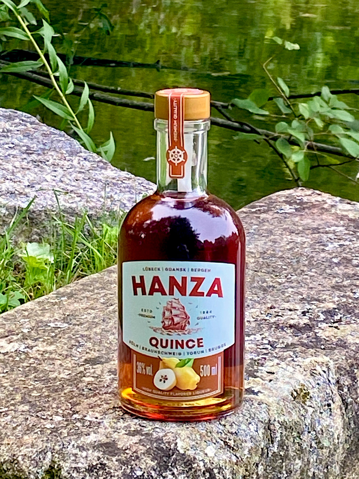 Hanza Quince Quittenlikör auf einem Felsen am See, Flasche mit Quittenmotiv und Segelschiff auf dem Etikett.