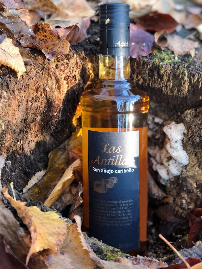 Flasche Las Antillas Ron Añejo Caribeño auf Holzfläche vor ruhigem See und unscharfem Hintergrund, 70 cl, 37,5 % Vol. Alkohol.