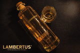 Lambertus Single Malt Whiskyflasche mit passendem Tumbler-Glas auf dunkler Oberfläche, goldene Reflexe im Licht
