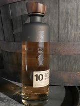 Lambertus 10 Years Founders Edition Whiskyflasche vor einem Holzfass, belgischer Single Grain Whisky mit Holzverschluss.