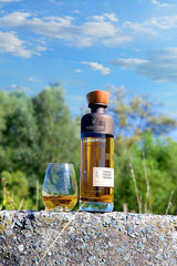 Lambertus Whiskyflasche und gefülltes Glas auf einer Steinmauer vor blauem Himmel und grünen Bäumen
