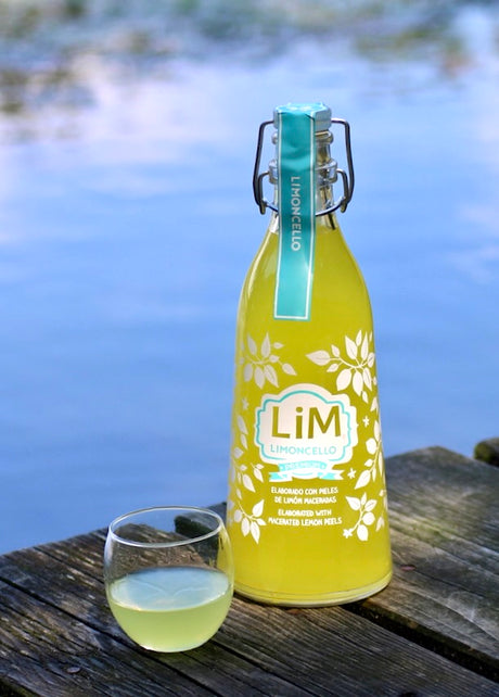 Lim Limoncello Flasche mit kleinem Glas auf Holzsteg vor blauem Wasser im Hintergrund