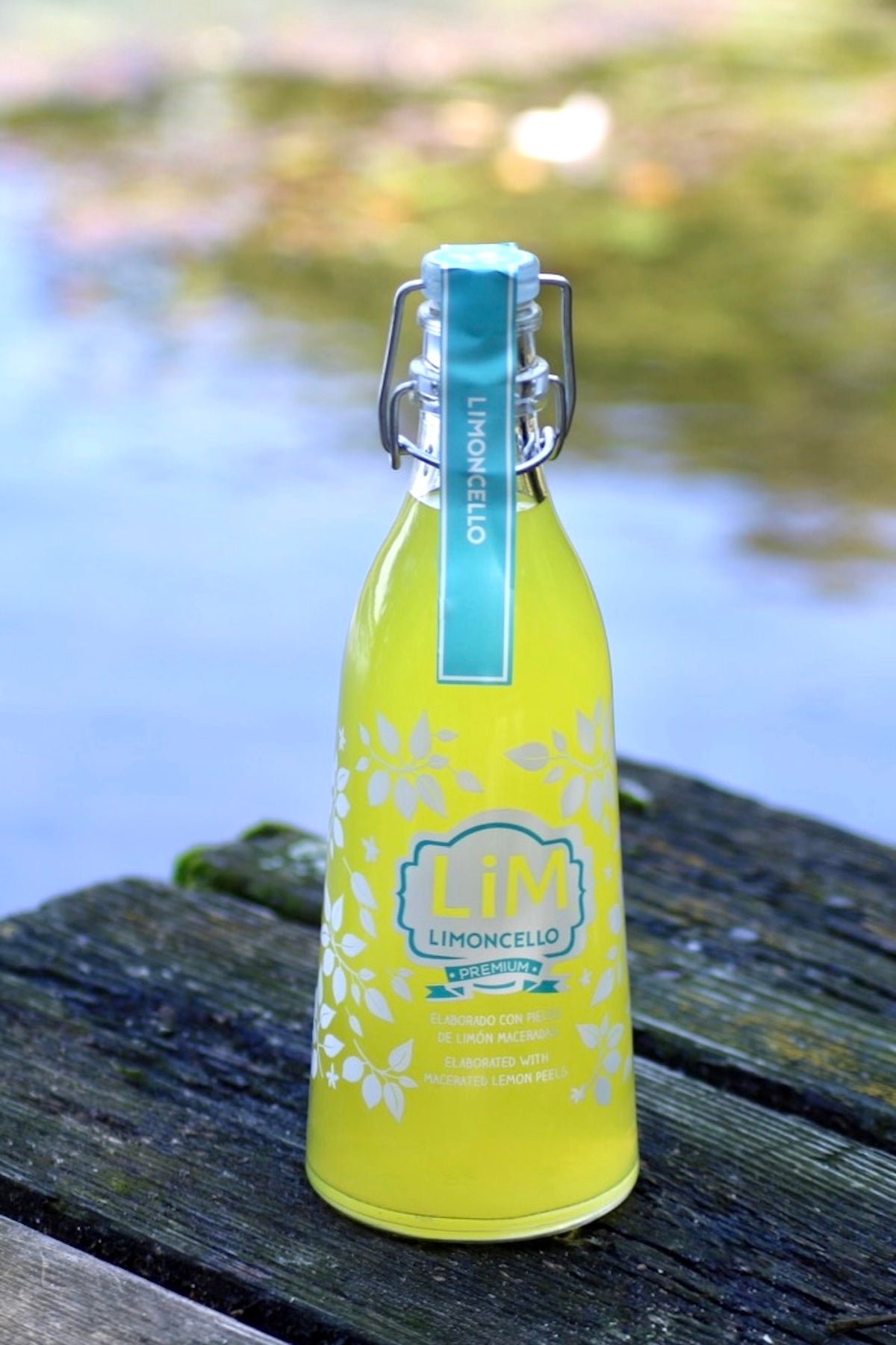 Lim Limoncello Likör in gelber Bügelflasche auf Holzsteg vor verschwommenem Wasserhintergrund