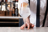  Elegantes Cocktailglas mit einer Gin-Tonic-Kreation, dekoriert mit frischen Apfelscheiben, präsentiert von einem Barkeeper im Hintergrund.