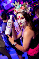 Frau mit farbenfrohem Gesichtsmuster und Blumenkranz hält eine Flasche Mex Maracuja-Tequila Sahnelikör auf einer Party.