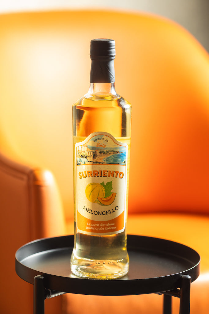Flasche Surriento Meloncello auf einem schwarzen Tisch vor einem orangefarbenen Stuhl.