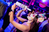 Frau mit kunstvoll bemaltem Gesicht und Blumenkranz hält eine Flasche Mex Maracuja-Tequila Sahnelikör auf einer Party.
