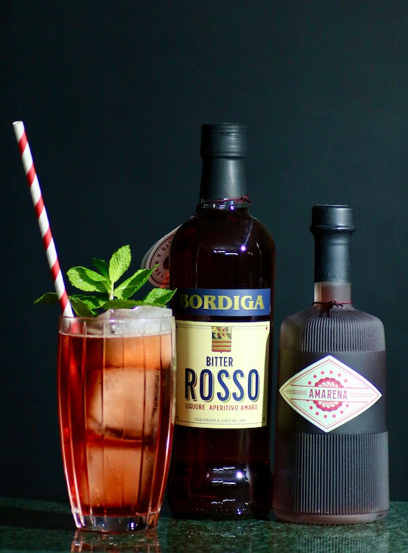 Nalgaa Cocktail mit Bitter Rosso Bordiga und Kirschlikör im Glas mit Eis, Minze und Strohhalm