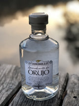 O’Carballo Orujo Flasche auf Holzfläche vor unscharfem Seehintergrund bei Sonnenuntergang, 70 cl, 40 % vol.