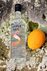 Flasche Triple Sec Charly’s auf hellem Felsgestein, daneben eine ganze Orange