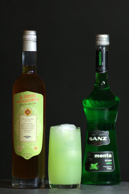 Perroquet Cocktail hellgrün im Glas zwischen Le Pastis du Liquoriste und Sanz Minzsirup auf dunklem Untergrund