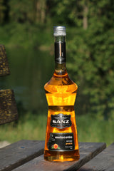 Sanz Pfirsichsirup in bernsteinfarbener Flasche auf Holzbank vor grünem Hintergrund