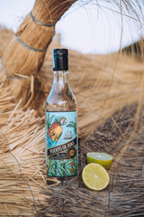 Flasche Puerto de Ayas weißer Rum auf trockenem Stroh mit zwei halben Limetten daneben.