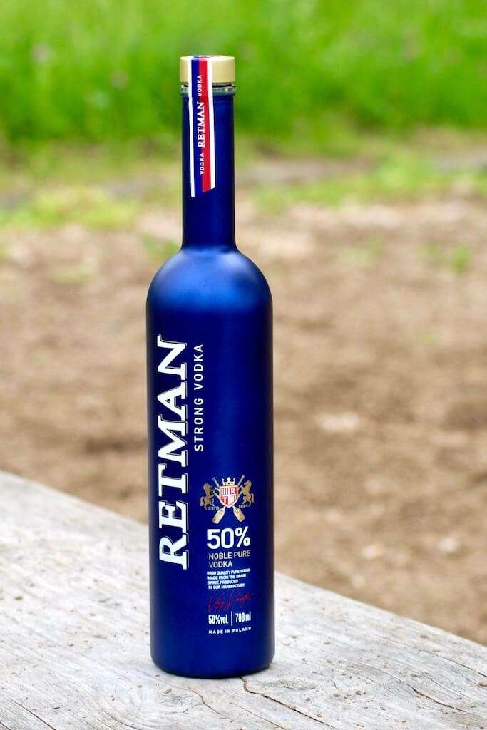 Retman Strong Vodka in blauer Flasche auf Holzuntergrund mit unscharfem Grün im Hintergrund.