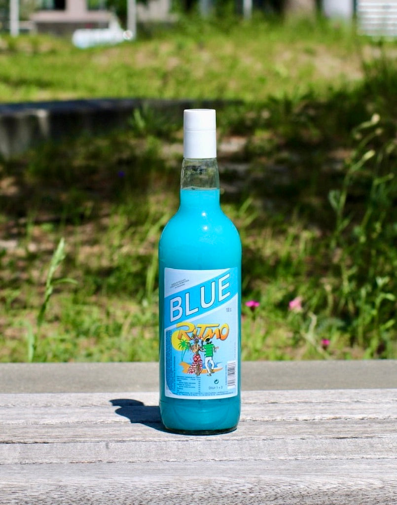 Flasche Ritmo Blue 1 L mit blauem Getränkekonzentrat und weißem Verschluss auf Holzbank im Sonnenlicht