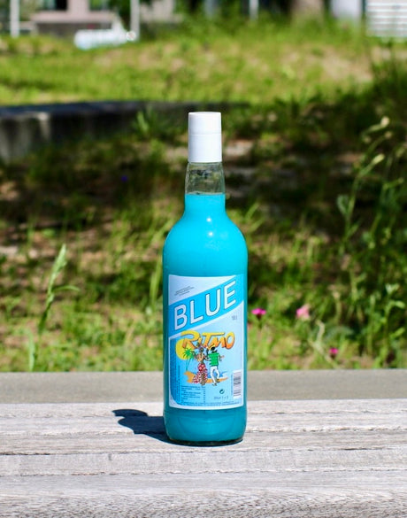 Flasche Ritmo Blue 1 L mit blauem Getränkekonzentrat und weißem Verschluss auf Holzbank im Sonnenlicht