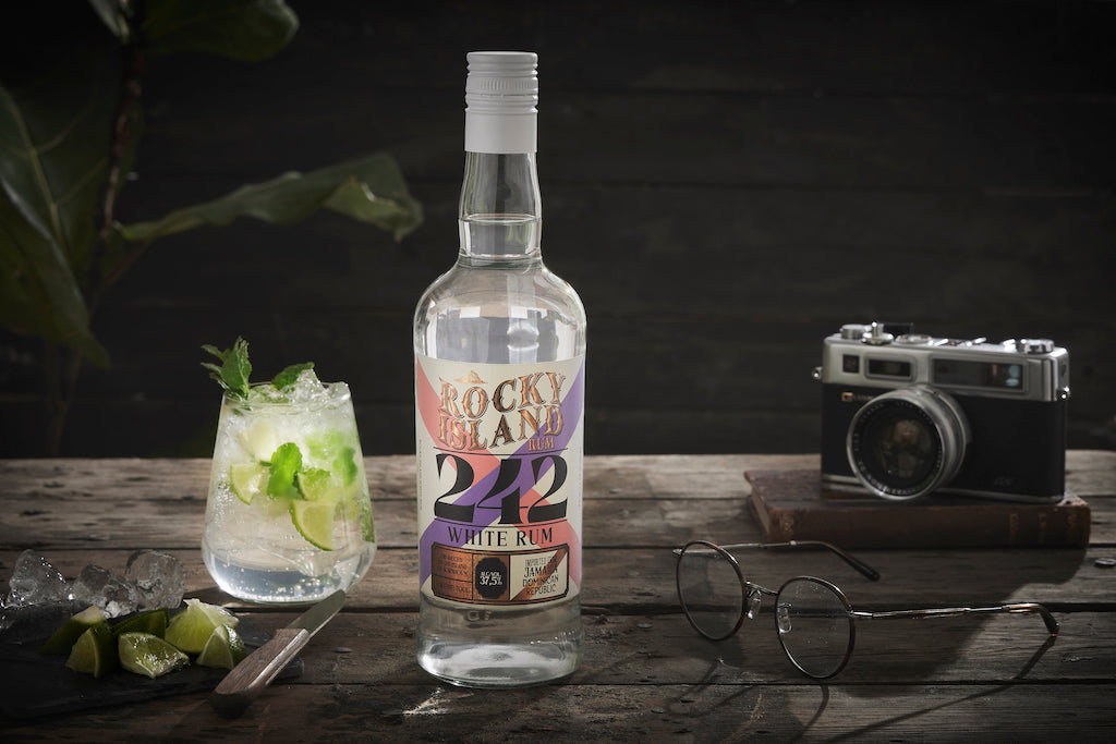Rocky Island 242 White Rum Flasche neben Rum-Cocktail mit Limette und Minze auf Holztisch