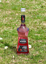 Sanz Rosensirup 700 ml, elegante Flasche mit schwarzem Etikett, auf einer grünen Wiese mit Gänseblümchen platziert.