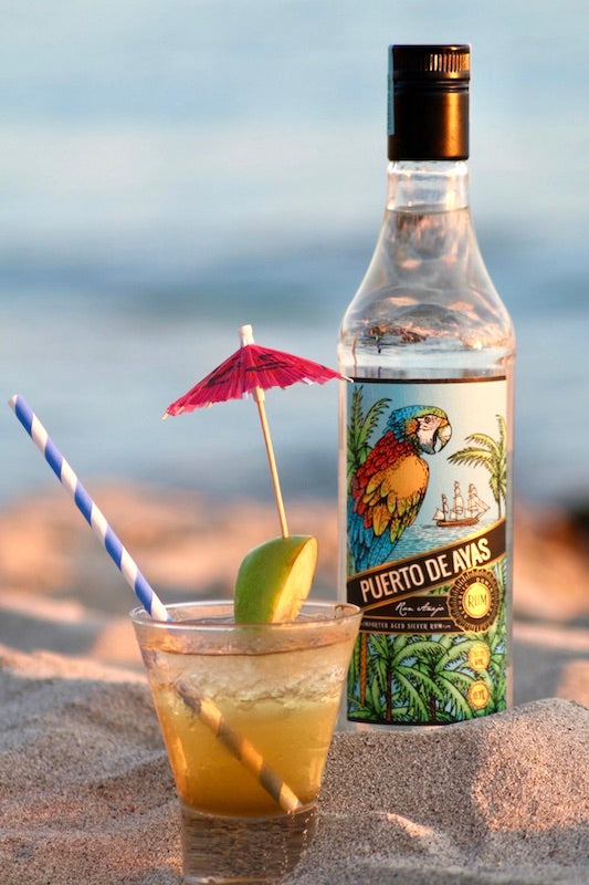 Rum-Apfel-Blend Cocktail mit Puerto de Ayas Rum, Apfelscheibe, Schirmchen und Strohhalm am Strand