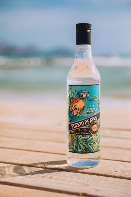 Puerto de Ayas Rumflasche auf Holztisch mit Meer und Himmel im Hintergrund.