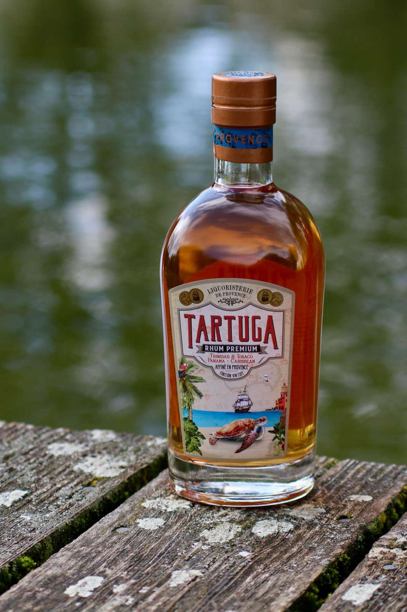 Tartuga Rhum Premium Flasche auf verwittertem Holzsteg mit Wasser im Hintergrund.