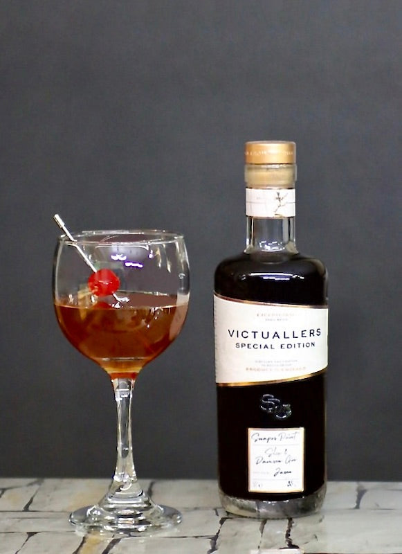 San Francisco Cocktail mit Sloe Gin Flasche und Cocktailkirsche vor dunklem Hintergrund