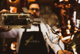 Schwangau Dry Gin wird aus einer Flasche in ein Glas der Brennerei Schroll eingeschenkt, im Hintergrund eine kupferne Destille.