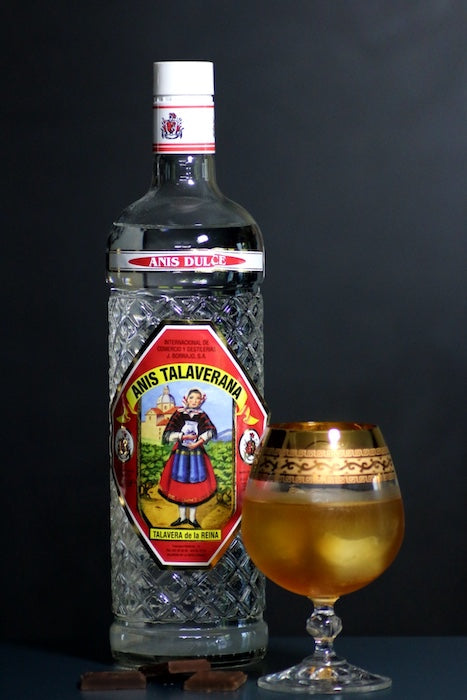 Sol y Sombra Cocktail mit Anis Talaverana Flasche, verziertem Glas und Schokolade vor dunklem Hintergrund