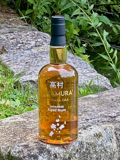 Takamura Japanese Aged Rum Punara Oak auf einem Felsen am See, goldfarbene Flasche mit japanischer Schrift.