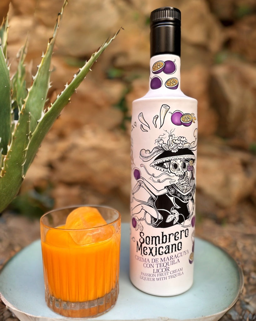Flasche Sombrero Mexicano Maracuja-Tequila-Likör mit Totenkopf-Design, neben einem Glas mit Eis auf einem Teller, dekoriert mit Agave.