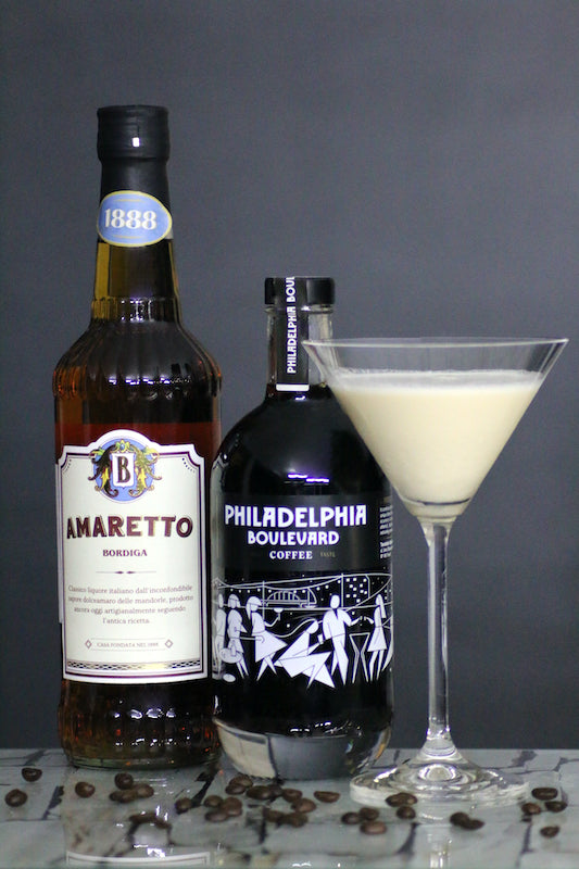 Amaretto und Kaffeelikör Flaschen neben Toasted Almond Cocktail im Martiniglas auf Tisch mit Kaffeebohnen