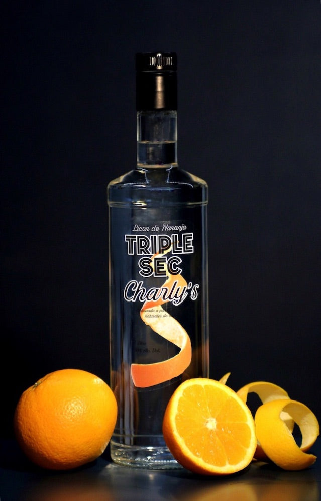 Flasche Triple Sec Charly’s vor dunklem Hintergrund mit ganzen Orangen, halber Orange und Orangenschalen.