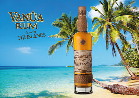 Flasche Vanua Rum Añejo vor tropischer Strandkulisse mit Palmen und türkisblauem Meer, Fiji-Inseln, 3-5 Jahre gereift.