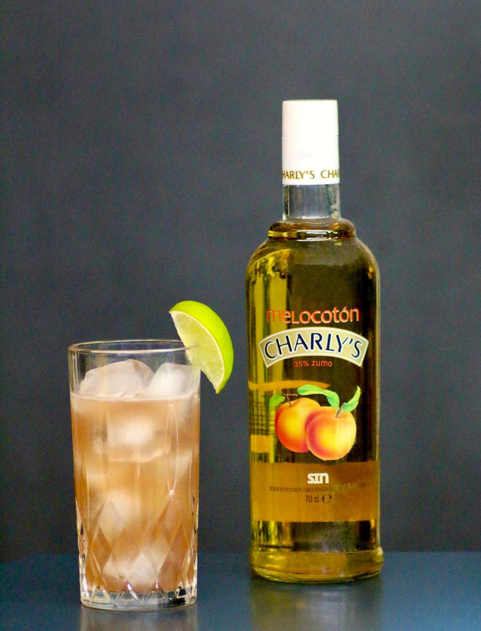 Alkoholfreier Woo Woo Cocktail mit Eiswürfeln und Limettenscheibe, daneben eine Flasche Charly’s Pfirsich.
