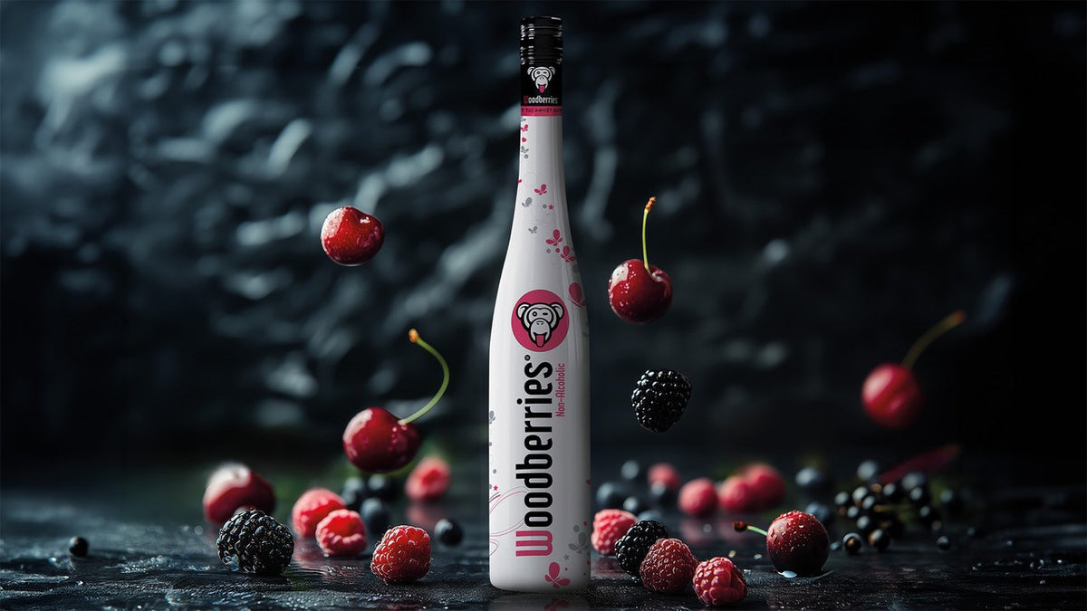 Woodberries Non-Alcoholic Flasche umgeben von Schwarzkirschen, Brombeeren, Himbeeren und schwarzen Johannisbeeren.
