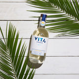 Flasche VITA Vodka auf weißem Holzhintergrund, umrahmt von grünen Palmblättern.